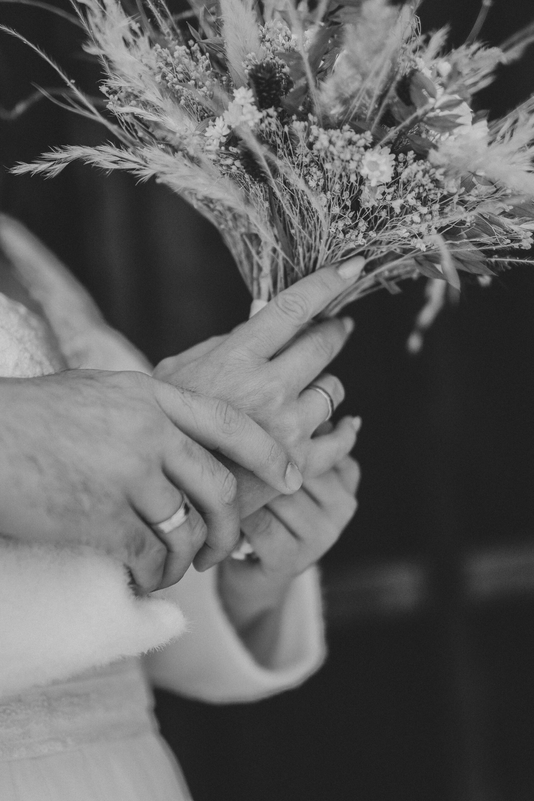 Hochzeitspaar hält gemeinsam den Brautstrauß. Bild in Graustufen und weiß